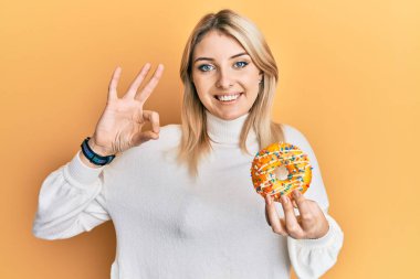 Kafkasyalı genç bir kadın donut tutuyor. Parmaklarıyla imza atıyor. Gülümsüyor. 