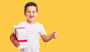 Küçük şirin çocuk elinde hediyeyle gururla bağırıyor zaferi ve başarıyı kutluyor. Kollarını kaldırıp heyecanla bekliyor. 