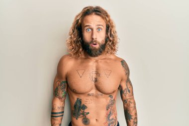 Sakallı, uzun saçlı, dövmeleri olmayan yakışıklı bir adam. Korkmuş ve şok olmuş bir ifade, korku ve heyecanlı bir yüz ifadesi var.. 