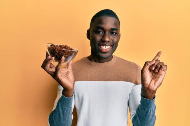Genç Afro-Amerikan adam elinde kuru üzümlü bir kaseyle mutlu bir şekilde elini ve parmağını kenarı işaret ediyor. 