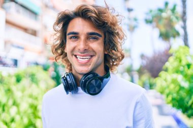 Genç, yakışıklı, gülümseyen, kulaklık takan, şehir sokaklarında yürüyen bir İspanyol.