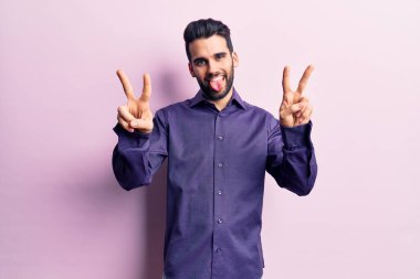 Sakallı, sıradan tişörtlü, ağzı açık bir şekilde gülümseyen, iki elini de zafer işareti yapan genç yakışıklı bir adam. İki numara.. 