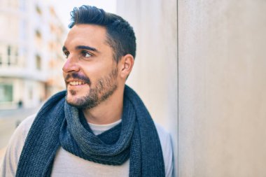 Genç İspanyol adam mutlu bir şekilde gülümsüyor. Şehrin duvarına yaslanmış bir eşarp takıyor.