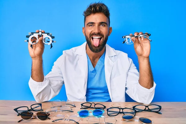 Jovem Hispânico Com Óculos Optometria Sentado Mesa Colando Língua Feliz — Fotografia de Stock