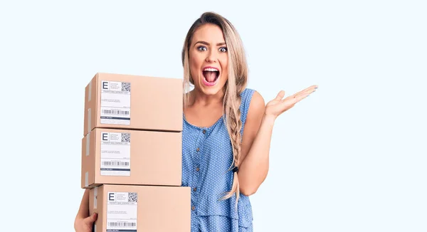 Young Beautiful Blonde Woman Holding Delivery Boxes Celebrating Victory Happy — Stock Photo, Image