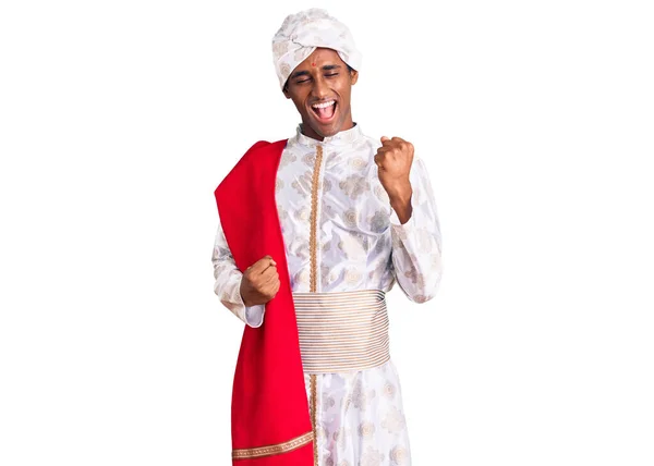 伝統的なシャーワニを身に着けているアフリカのハンサムな男は腕を上げて目を閉じて成功のために驚きと驚きを祝う服を見た 勝者のコンセプト — ストック写真