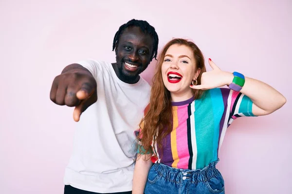 Interracial couple wearing casual clothes smiling doing talking on the telephone gesture and pointing to you. call me.