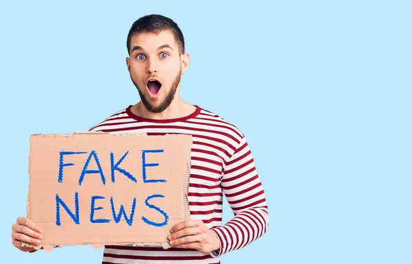 Young Handsome Man Holding Fake News Message Banner Scared Amazed — Stock Photo, Image