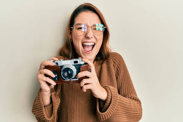 Young caucasian woman holding vintage camera celebrating crazy and amazed for success with open eyes screaming excited.