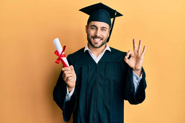 Jovem Hispânico Homem Vestindo Graduação Roupão Segurando Diploma Fazendo Sinal — Fotografia de Stock