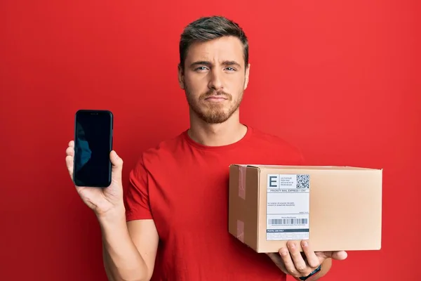 Yakışıklı Beyaz Adam Teslimat Paketini Tutuyor Akıllı Telefon Ekranını Depresif — Stok fotoğraf