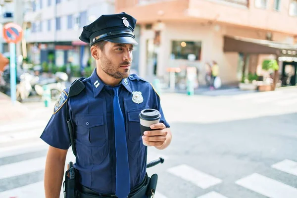 真剣な表情で警察制服を着た若いヒスパニック系の警官 町の通りに立ちコーヒーを飲みながら — ストック写真