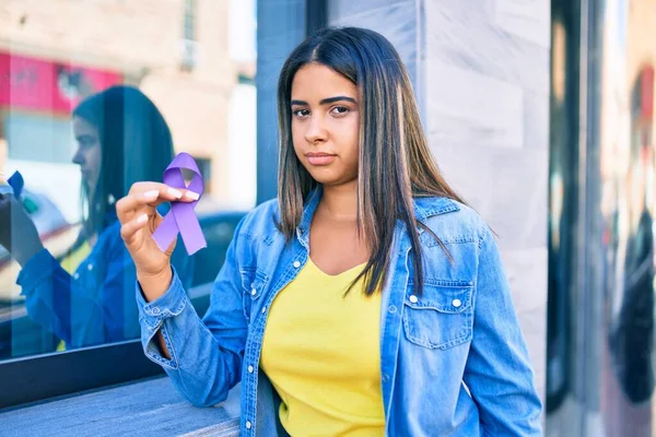 Young latin woman with serious expression holding purple ribbon at city.