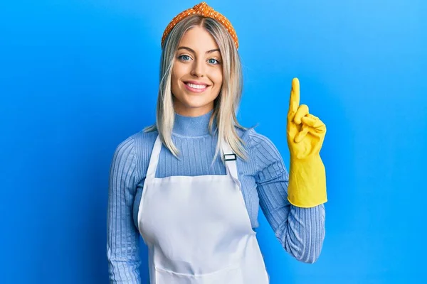 Beautiful Blonde Woman Wearing Cleaner Apron Gloves Showing Pointing Finger — Stock Photo, Image