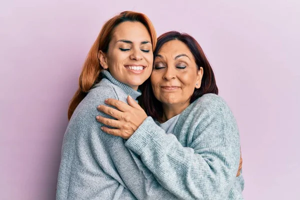 西班牙裔母亲和女儿高兴地微笑着 拥抱着孤零零的粉红背景 — 图库照片