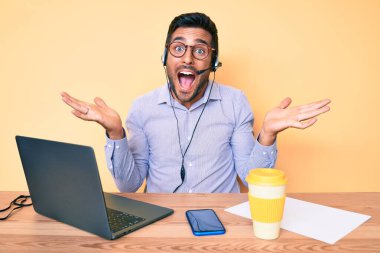 Çağrı merkezindeki operatör kulaklığı takarak masada oturan İspanyol genç adam zaferi mutlu bir gülümsemeyle ve ellerini kaldırarak kutluyor. 