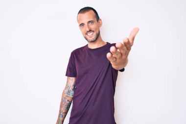 Dövmeli genç, sıradan kıyafetler giyen, dostça gülümseyen, selamlaşmak ve selamlamak için el sıkışan yakışıklı adam. başarılı iş. 