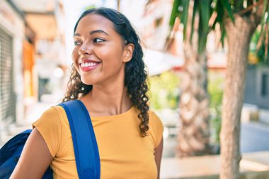 Genç Afrikalı Amerikalı öğrenci kampüste mutlu bir şekilde yürürken gülümsüyor..