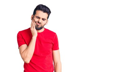 Sakallı, sıradan tişörtler giyen, diş ağrısı ya da diş hastalığından dolayı ağızlarına acı dolu bir ifadeyle dokunan genç yakışıklı bir adam. dişçi 