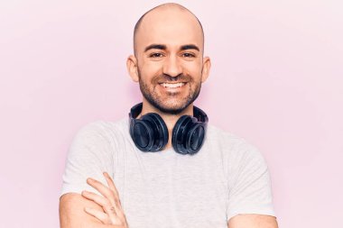 Genç yakışıklı kel adam kulaklık takarak müzik dinliyor kollarını kavuşturup kameraya bakıyor. pozitif kişi. 