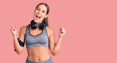 Spor kıyafetleri giyen, kulaklık takan genç ve güzel bir İspanyol kadın kollarını kaldırarak ve açık gözlerle başarıyı kutluyor. Kazanan konsept. 