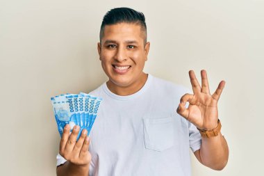 On bin Şili pezosu tutan genç Latin adam parmaklarıyla imza atıyor, gülümseyerek mükemmel bir sembol oluşturuyor. 