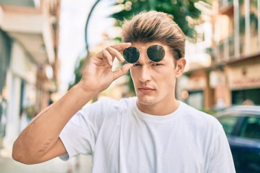 Şehirde yürüyen, ciddi bir ifadeye sahip beyaz bir genç..