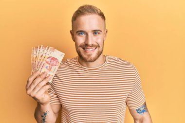 Meksika pezosu tutan beyaz bir genç. Olumlu ve mutlu görünüyor. Kendine güvenen bir gülümsemeyle dişlerini gösteriyor. 