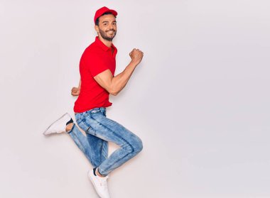 Mutlu gülümseyen üniformalı yakışıklı İspanyol teslimatçı. Yüzünde tebessümle zıplıyor, beyaz arka planda yumruklar havada kutluyor..