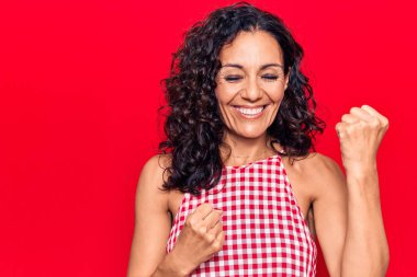 Orta yaşlı, kolsuz tişört giyen güzel bir kadın kolları havada ve gözleri kapalı bir şekilde başarıyı kutluyor ve şaşırıyor. 