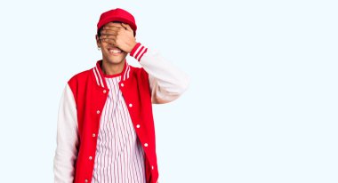 Beyzbol üniforması giyen genç Afro-Amerikan bir adam. Gülümsüyor ve elleri yüzlerinde, şaşkınlıktan gözleri kapatıyordu. kör kavram. 