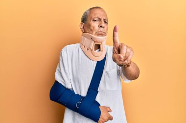 Servikal tasma ve kol takan yakışıklı ve olgun bir adam parmağını kaldırmış ve kızgın bir ifadeyle işaret ediyor. Hiç hareket göstermiyor. 