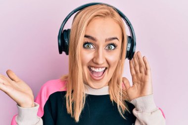 Güzel beyaz kadın müzik dinliyor kulaklıkla başarıyı kutluyor mutlu bir gülümsemeyle ve kazanan el kaldırarak ifade ediyor. 