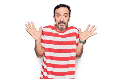 Orta yaşlı, çizgili tişört giyen yakışıklı bir adam izole edilmiş beyaz arka planda duruyor ve kolları açık, hiçbir fikri ve şüpheli bir yüzü yok..