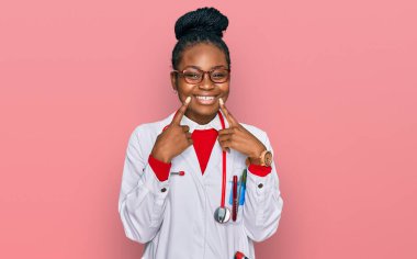 Genç Afro-Amerikan kadın doktor üniforması ve steteskop giymiş ağzı açık gülümseyen, parmakları işaret eden ve neşeli gülümsemeye zorlayan. 