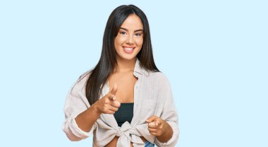 Gündelik giysiler giymiş genç, güzel İspanyol kız mutlu ve komik yüzüyle kamerayı işaret ediyor. iyi enerji ve titreşimler. 