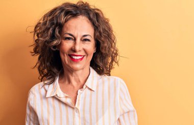 Orta yaşlı, esmer, çizgili tişört giyen, mutlu ve havalı bir gülümsemeyle sarı arka planda duran güzel bir kadın. Şanslı kişi..