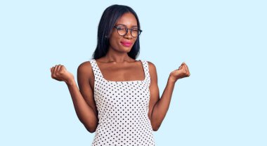 Genç Afro-Amerikalı kadın, günlük kıyafetler ve gözlük takıyor çok mutlu ve heyecanlı, kazanan jestler yapıyor, kolları havada, gülümsüyor ve başarı için bağırıyor. kutlama konsepti. 