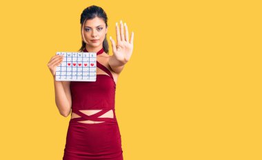 Genç ve güzel bir kadın kalp takvimini açık elle tutuyor dur işareti yapıyor ciddi ve kendinden emin bir ifadeyle, savunma hareketi yapıyor. 