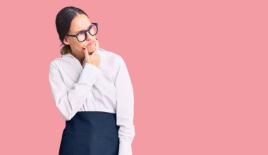 Profesyonel garson önlüğü giyen güzel esmer bir kadın bir soru hakkında endişeli ve gergin bir şekilde düşünüyor. 