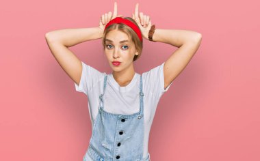 Kafkasyalı genç bir kız, günlük kıyafetler giyip parmaklarını boynuzlarına geçirip komik jestler yapıyor. 