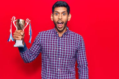 Genç latin adam elinde kupa tutuyor. Korkmuş ve ağzı açık kalmış, şaşırmış ve şaşırmış. 