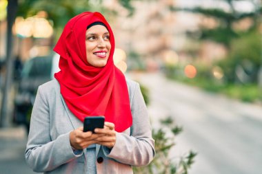 Şehirde akıllı telefon kullanan tesettürlü genç Arap iş kadını..