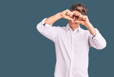 İş kıyafetleri ve gözlük takan genç yakışıklı adam kalp şeklinde el ve parmaklarıyla tabelanın içinden bakıp gülümsüyor. 