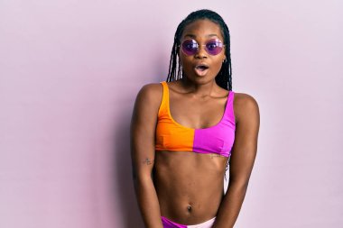 Genç Afro-Amerikan kadın bikini ve güneş gözlüğü takıyor. Şaşırtıcı bir ifade, korku ve heyecan dolu bir yüz ifadesi var.. 