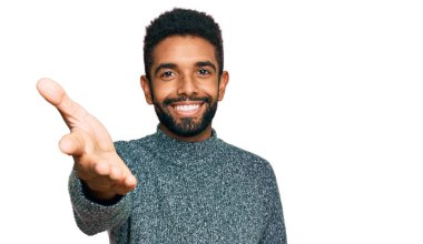 Genç Afro-Amerikan adam günlük kıyafetler giyip gülümseyerek dostça el sıkışarak selamlama ve hoş geldin diyor. başarılı iş. 