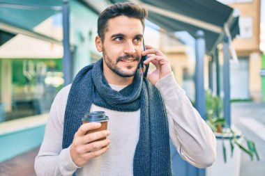 Genç İspanyol adam gülümsüyor. Akıllı telefonla konuşuyor ve şehirde kahve içiyor..