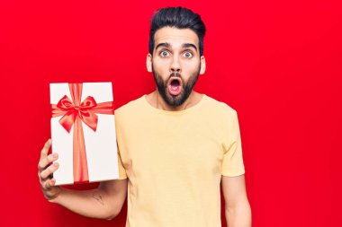 Sakallı, genç ve yakışıklı bir adam. Korkmuş ve ağzı açık kalmış, şaşırmış ve şaşırmış. 