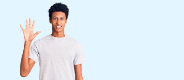 Genç Afro-Amerikalı günlük kıyafetler giymiş beş numarayı gösterip işaret ederken kendinden emin ve mutlu bir şekilde gülümsüyor.. 