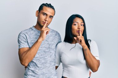 Gündelik kıyafetler giyen genç latin çift parmakları dudaklarında sessiz olmak istiyorlar. sessizlik ve gizli konsept. 